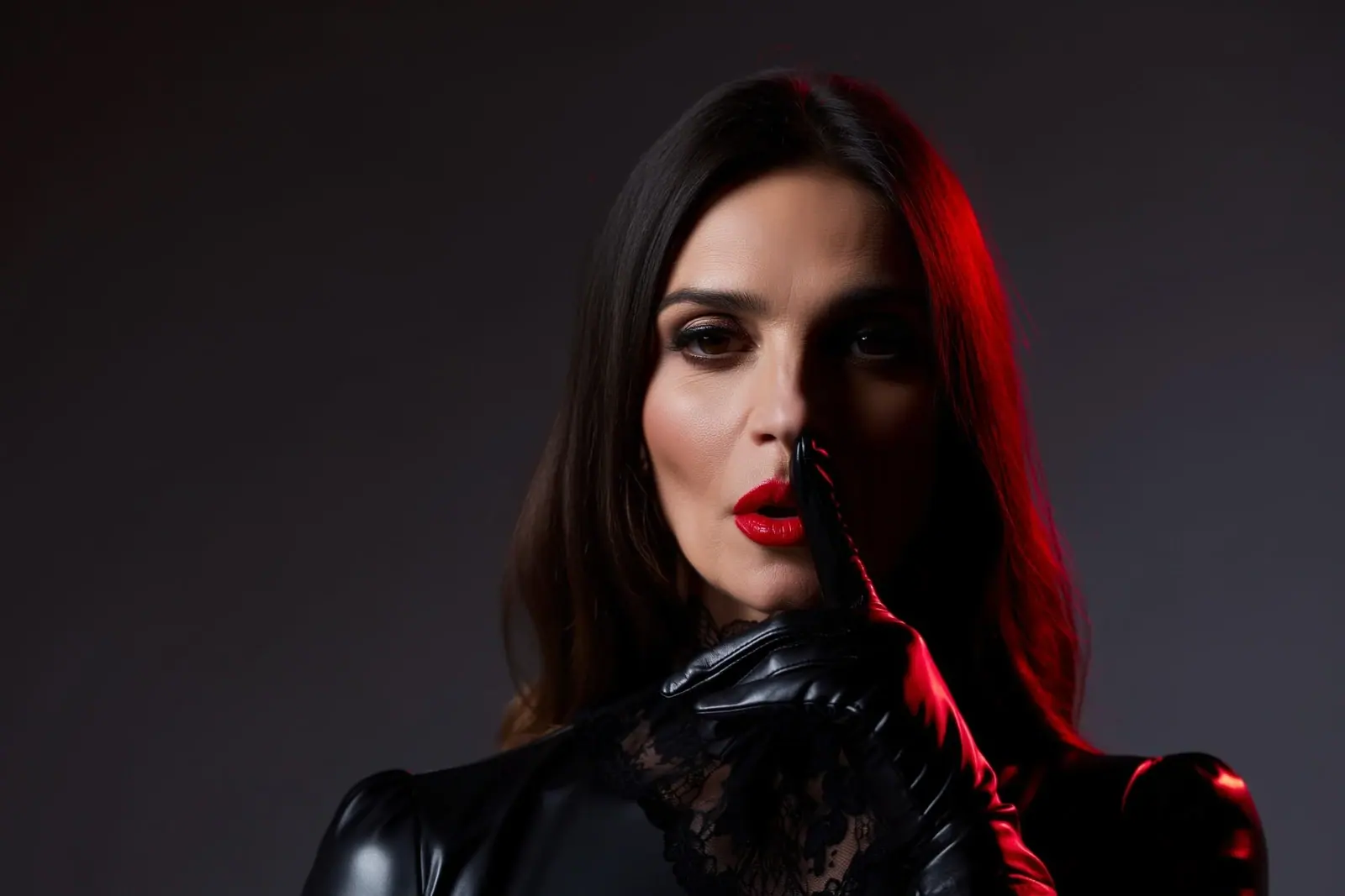 Domina-Telefonsex anonym: Frau legt einen behandschuhten Finger an die roten Lippen, eine Gesichtshälfte im Schatten